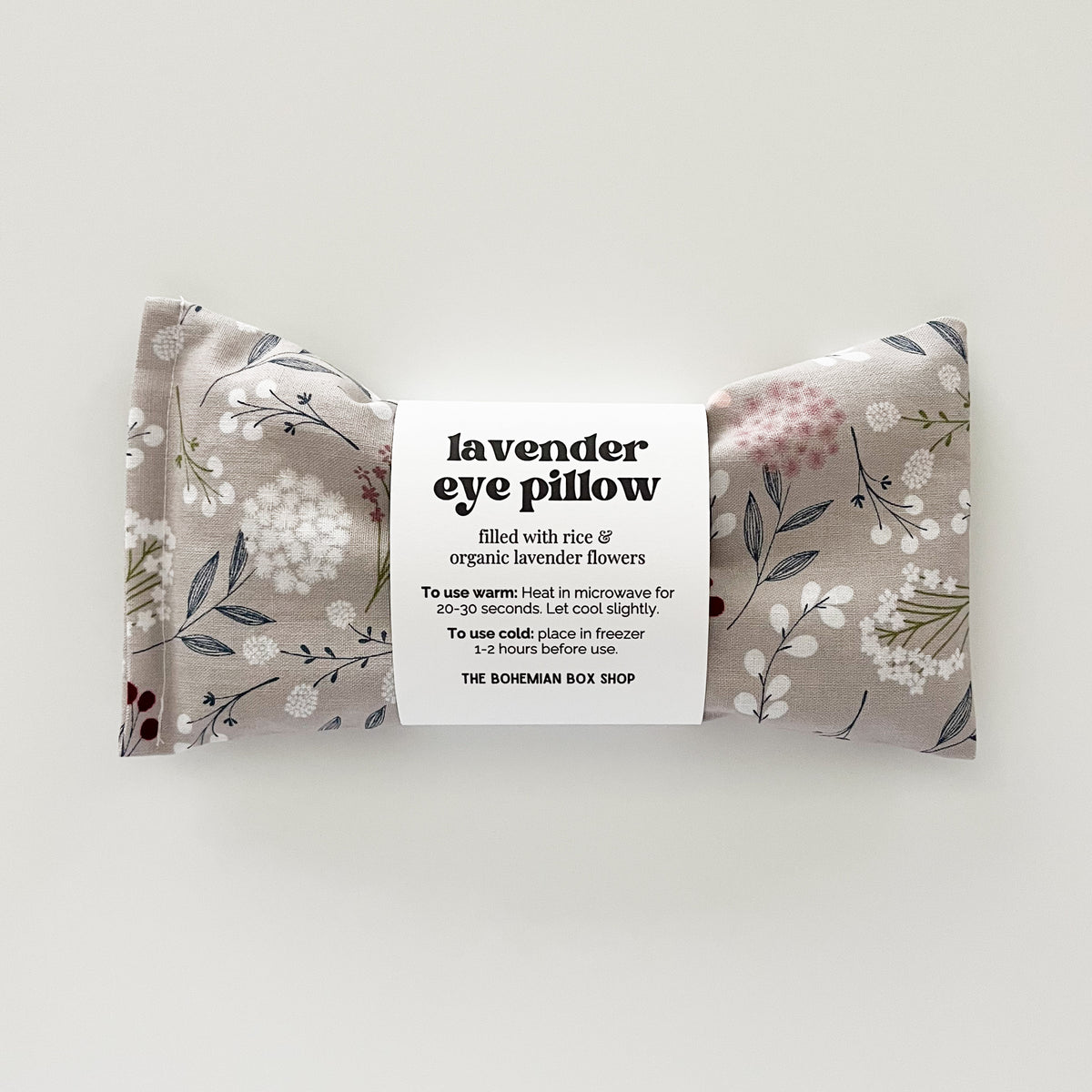A rectangular gray floral eye pillow with a label in the center that reads 'Lavender Eye Pillow' and includes product details.