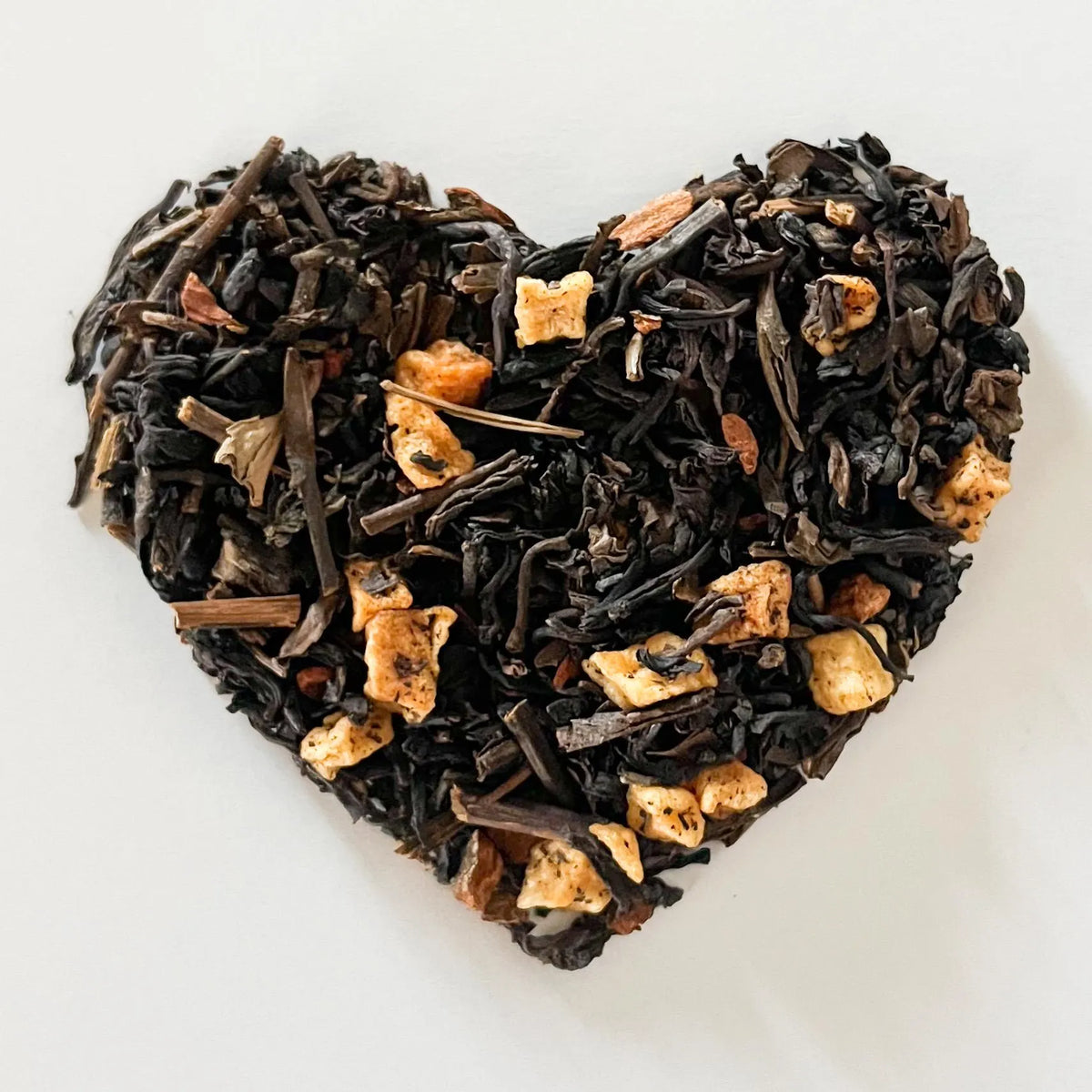 Heart-shaped arrangement of black tea leaves and gold pieces on a white background