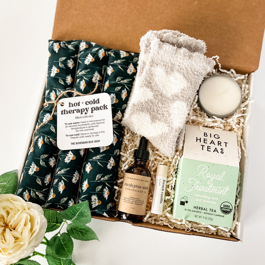 Gorgeous floral spa gift box containing hot and cold therapy pack, eucalyptus mint body oil, French vanilla lip balm, royal treatment big hear tea co tea, soy candle, and gray heart cozy socks for women.