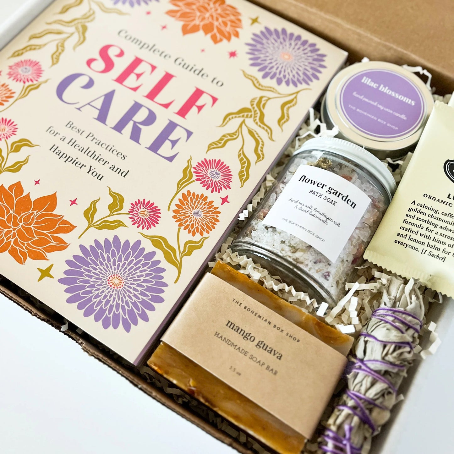 Self-care gift set for women. Includes a complete guy to self-care book, lilac soy candle, flower garden bath soak mango guava soap, tea packets, and mini sage bundle. 