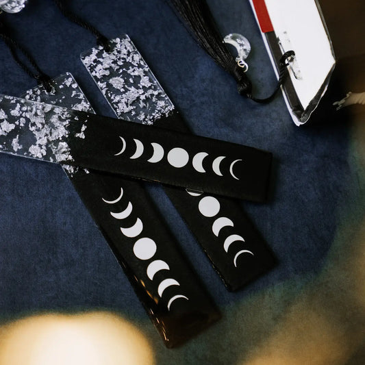 A black and silver resin bookmark with moon phase designs, displayed on a blue surface.
