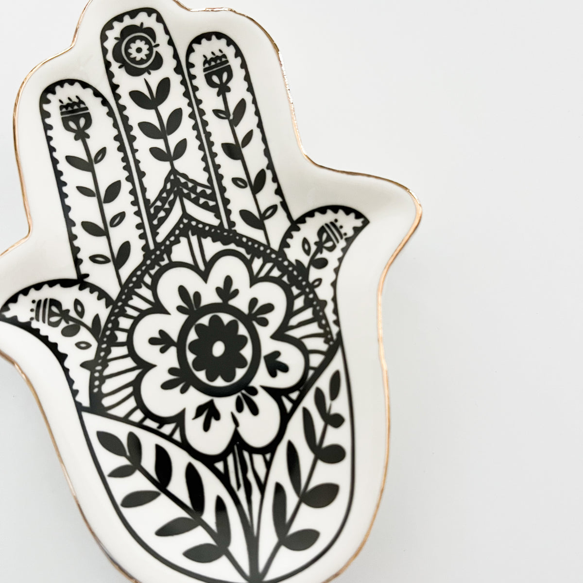 A black and white ceramic jewelry tray in the shape of a palm with gold trim, featuring a floral pattern in the center.