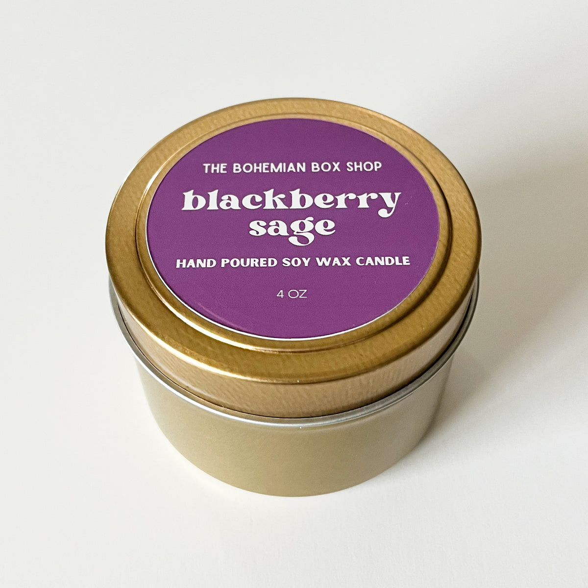 Blackberry Sage Soy Candle in a tin with a purple label from The Bohemian Box Shop on a white background