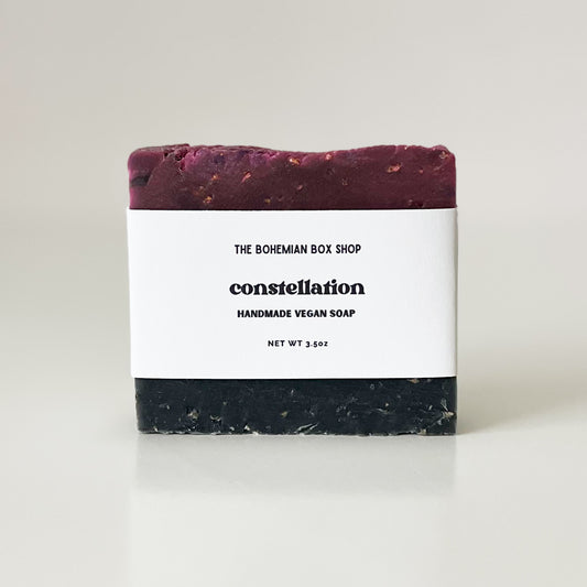 A purple handmade vegan soap bar with 'The Bohemian Box Shop' and 'CONSTELLATION' written on the packaging, indicating the scent of the soap.
