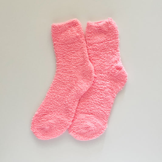 A pair of fluffy, textured pink socks laid flat on a white background.