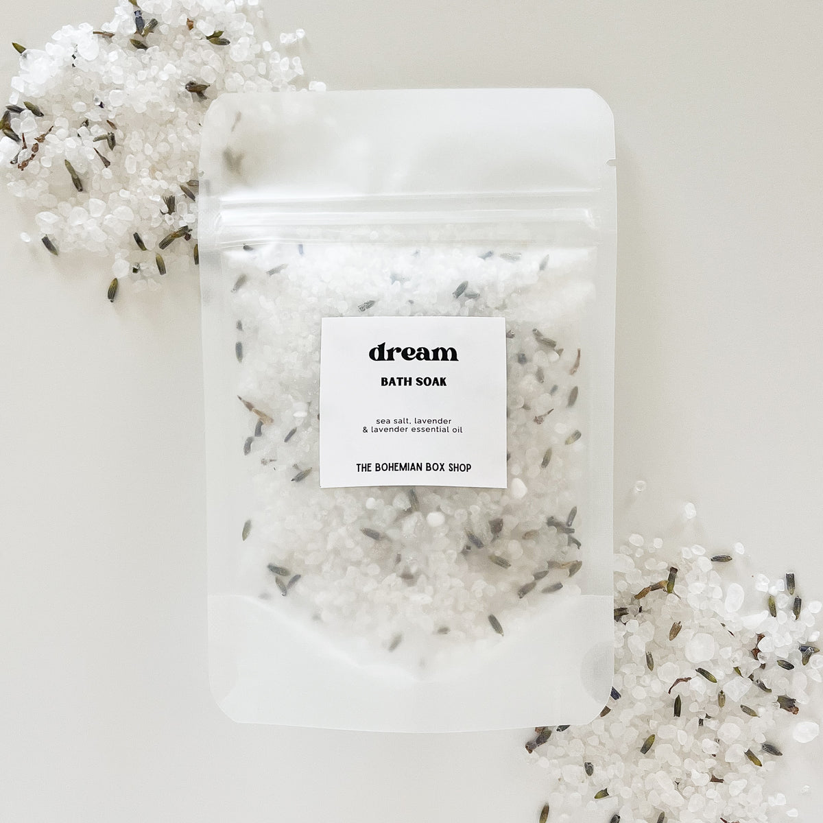 A sealed clear plastic packet labeled 'dream' containing white bath soak packets against a white background, with decorative lavender flowers scattered around.