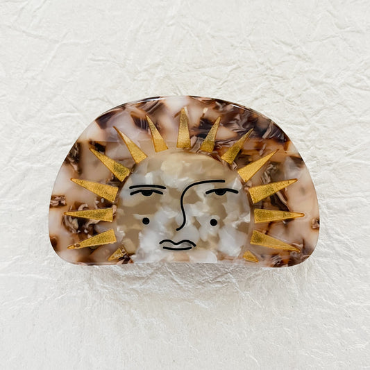 A hair claw with a sun and face design, primarily in brown tones with gold accents.