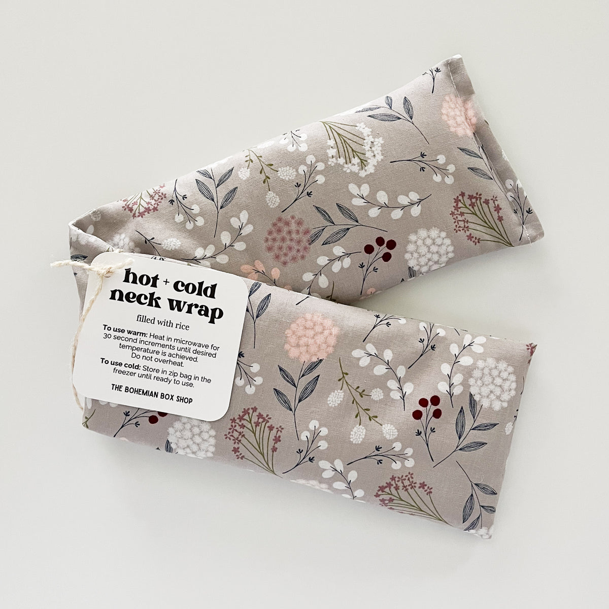 A floral patterned hot and cold neck wrap made of cotton, with a tag indicating it is from The Bohemian Box Shop.