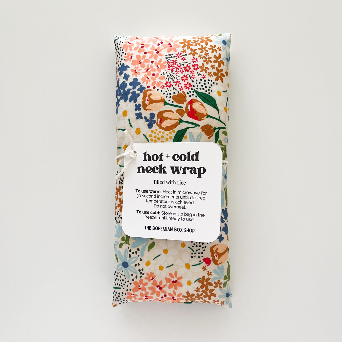 A packaged hot and cold neck wrap by The Bohemian Box Shop, featuring a colorful floral pattern on a white background with a white paper label in the center.