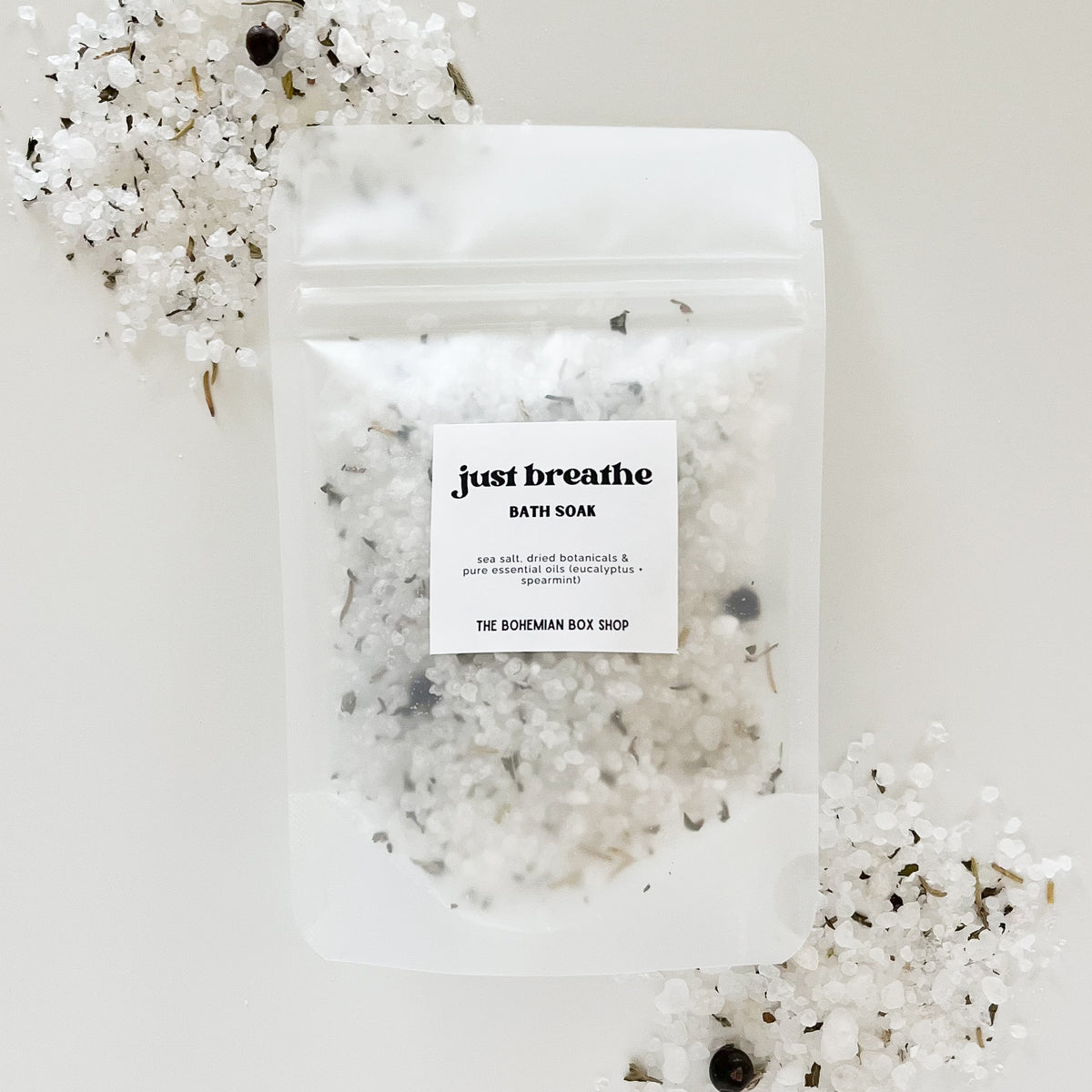 A packet of 'Just Breathe - Eucalyptus Mint Bath Soak' on a white surface surrounded by dried eucalyptus leaves and flowers made by The Bohemian Box Shop