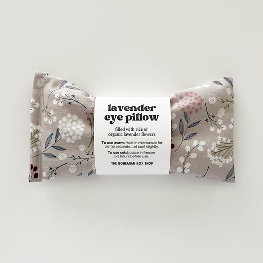 A rectangular gray floral eye pillow with a label in the center that reads 'Lavender Eye Pillow' and includes product details.