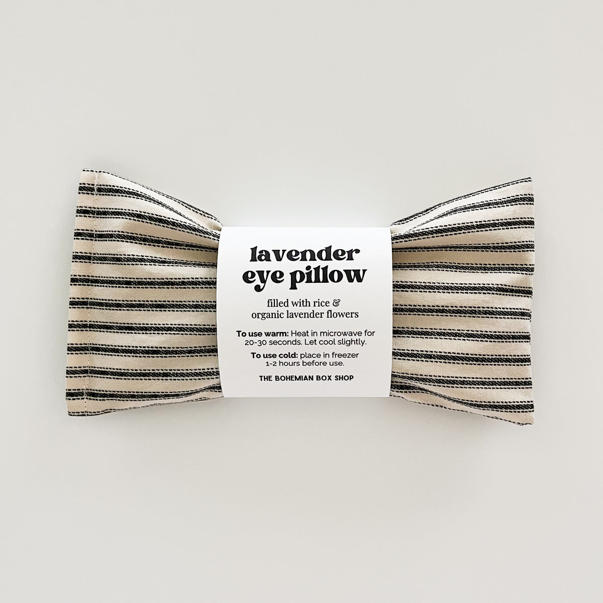 lavender eye pillow filled with rice and organic lavender flowers in an ivory and black stripe fabric on a white background