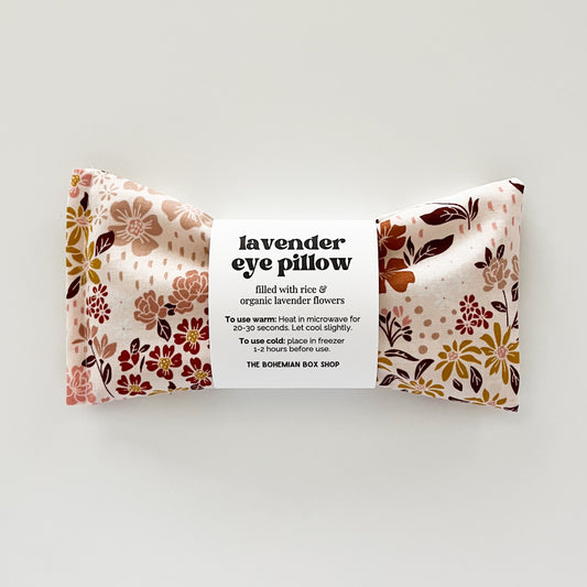A rectangular eye pillow with a floral pattern in earth tones, labeled 'Lavender Eye Pillow' filled with organic lavender flowers and rice. Made by The Bohemian Box Shop