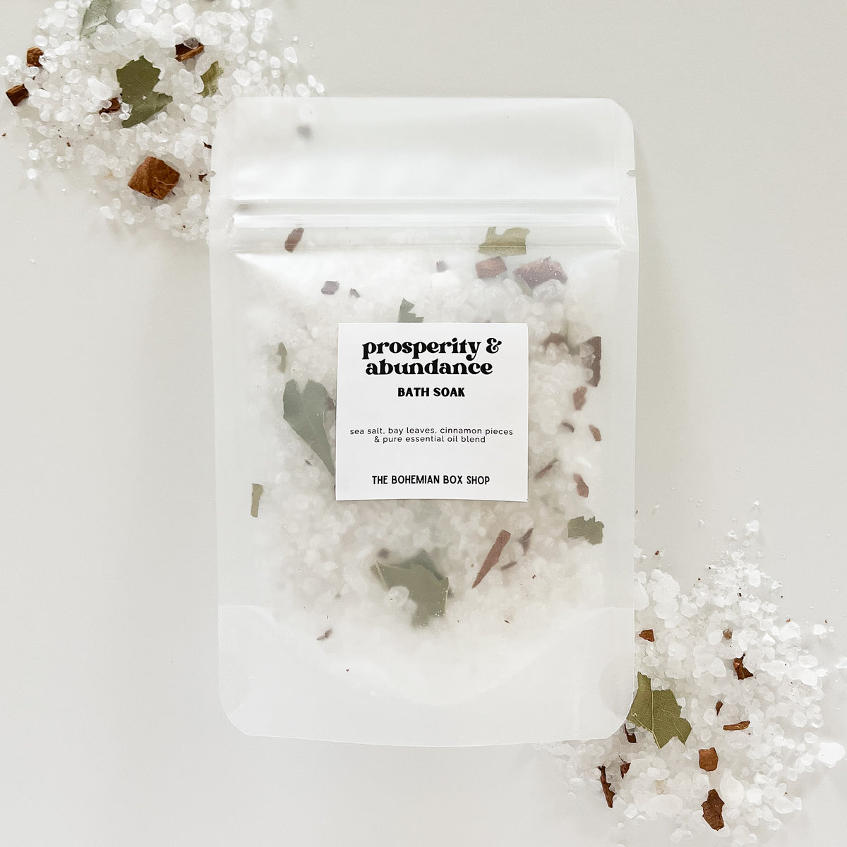 Prosperity and Abundance Bath Soak made by The Bohemian Box Shop surrounded by bath salts and dried herbs on a white background
