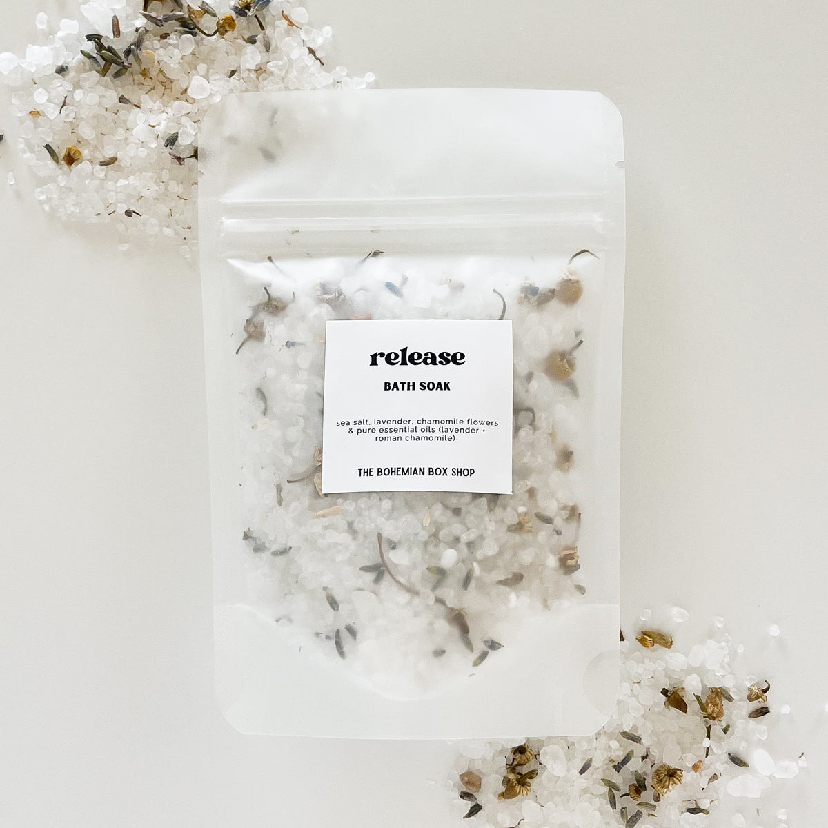 release bath soak made by The Bohemian Box Shop on a white background surrounded by bath salts and dried chamomile and lavender flowers