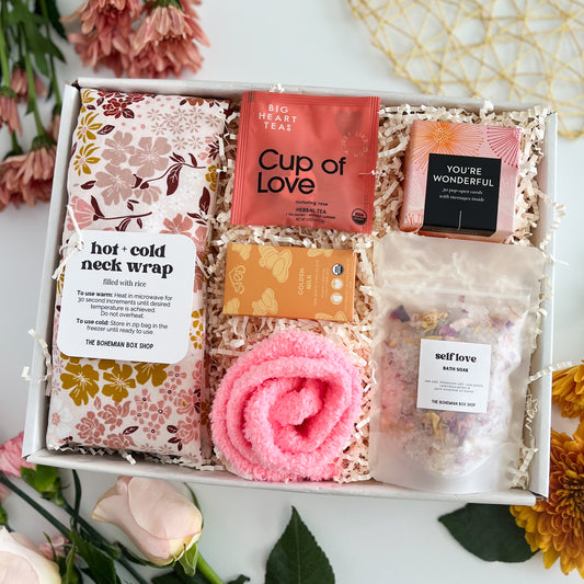 A curated gift box set from The Bohemian Box Shop containing a floral neck wrap, Big Heart Tea 'Cup of Love' herbal tea, a 'You're Wonderful' affirmation card pack, a self love bath soak, women's pink socks, sted chocolate bar arranged in a white box with shredded paper