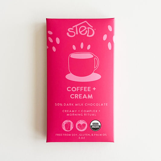 A pink package of Sted Coffee + Cream chocolate bar, featuring a white coffee cup graphic and text indicating 50% dark milk chocolate, on a clean white background.