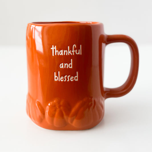 An orange ceramic mug with a pumpkin textured base and the words 'thankful and blessed' embossed on the front, set against a plain white background.