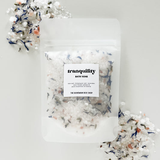 tranquility bath soak packet made by The Bohemian Box Shop on a white background surrounded by bath salts and dried botanicals