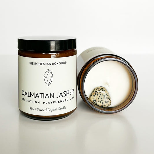 A jar of Dalmatian Jasper soy candle next to another candle with a dalmatian jasper crystal on top of the wax